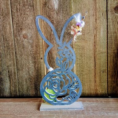 Dekorative Figur eines Hasen mit einer Blumendekoration vor rustikalem Holz.
