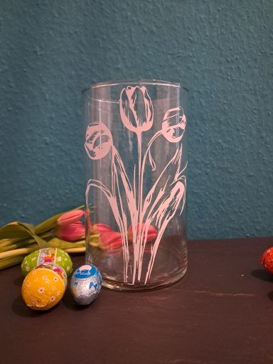 Vase mit Tulpenmotiv, umgeben von bunten Ostereiern.