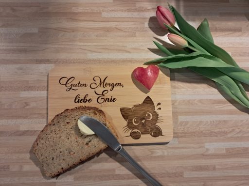 Ein Holzbrett mit einem Kätzchen-Motiv, Brot, Butter und Tulpen.