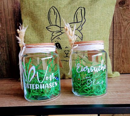 Zwei dekorative Gläser mit Aufschriften und grünem Gras im Inneren.
