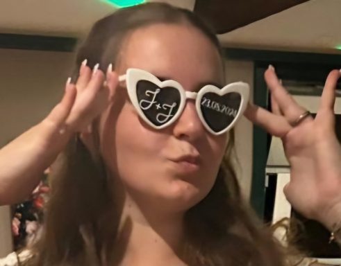 Frau mit Herzform-Sonnenbrille, posiert und zeigt ein Peace-Zeichen.