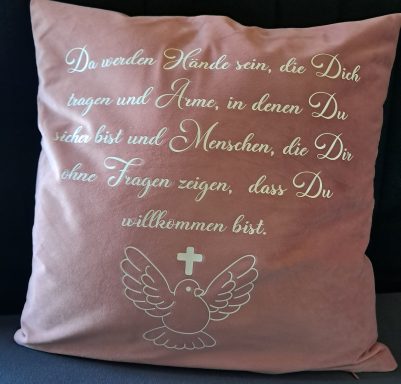 Rosa Kissen mit einem religiösen Text und einer Taube, die einen Kreuz darstellt.