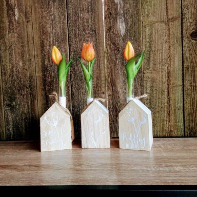 Drei Holzfiguren in Form von Häusern mit orangefarbenen Tulpen als Dekoration.