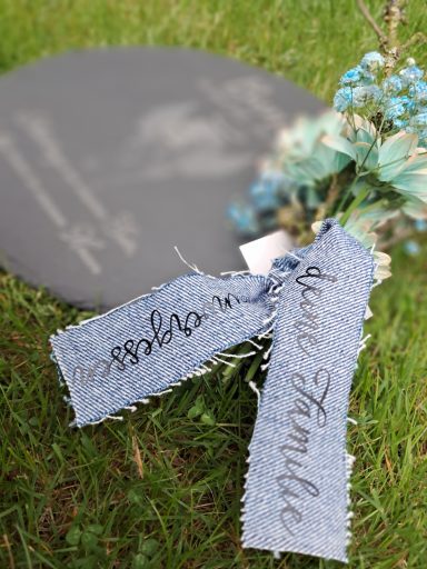 Ein grauer Grabstein mit einer blauen Blüte und einem Schild mit den Worten „liebe Familie“.
