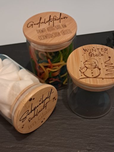Drei Behälter mit Holzdeckeln, gefüllt mit Süßigkeiten, Zucker und farbigen Gummibärchen.