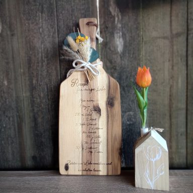 Holzbrett mit dekorativer Blumenarrangierung und einer kleinen Vase mit einer Tulpe.