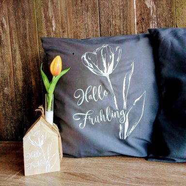Dekorative Kissen mit Blumenmotiv und einer Tulpe in einer Vase, beschriftet "Hallo Frühling".