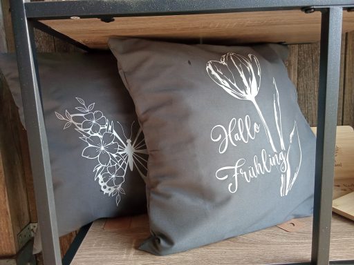 Zwei dekorative Kissen auf einem Regal, eines mit Lavendelmotiven und das andere mit Tulpen.