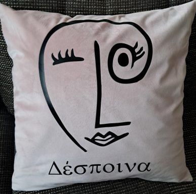 Kissen mit stilisiertem Gesicht und dem Wort „Δέσποινα“ in Schwarz auf rosa Hintergrund.