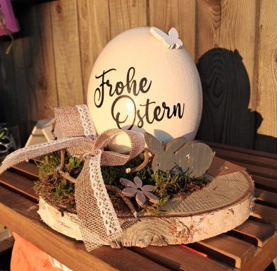 Dekoratives Osterarrangement mit einem großen Ei und Blumen auf einem Holztisch.