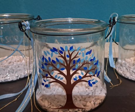 Drei Glasgefäße mit einem braunen Baum und blauen Blättern, gefüllt mit weißen Steinen.