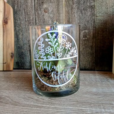 Glas mit Pflanzen und Blumenmustern auf einem rustikalen Holzuntergrund.