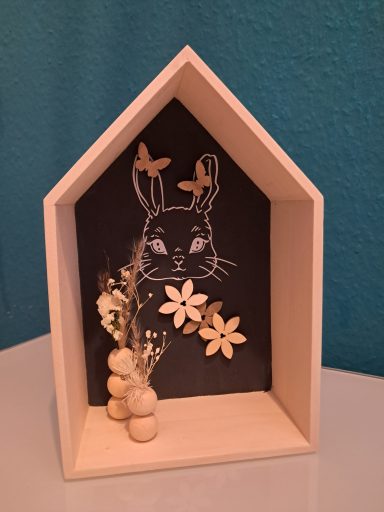 Holzkasten in Form eines Hauses mit einer Hasenzeichnung und dekorativen Blumen.