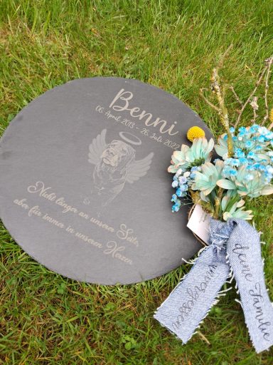 Gedenktafel mit dem Namen "Bennit" und einem Strauß aus Blumen und Bändern.