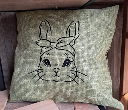 Kissen mit einer gestickten Hasenmaske und einem Kopftuch.