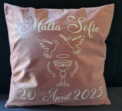 Rosa Kissen mit weißen Verzierungen: Tauben, Kelch und dem Namen "Malia-Sofie" sowie Datum.